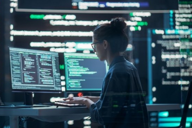 Programmiererin vor Bildschirmen mit Codes in dunklem Umfeld